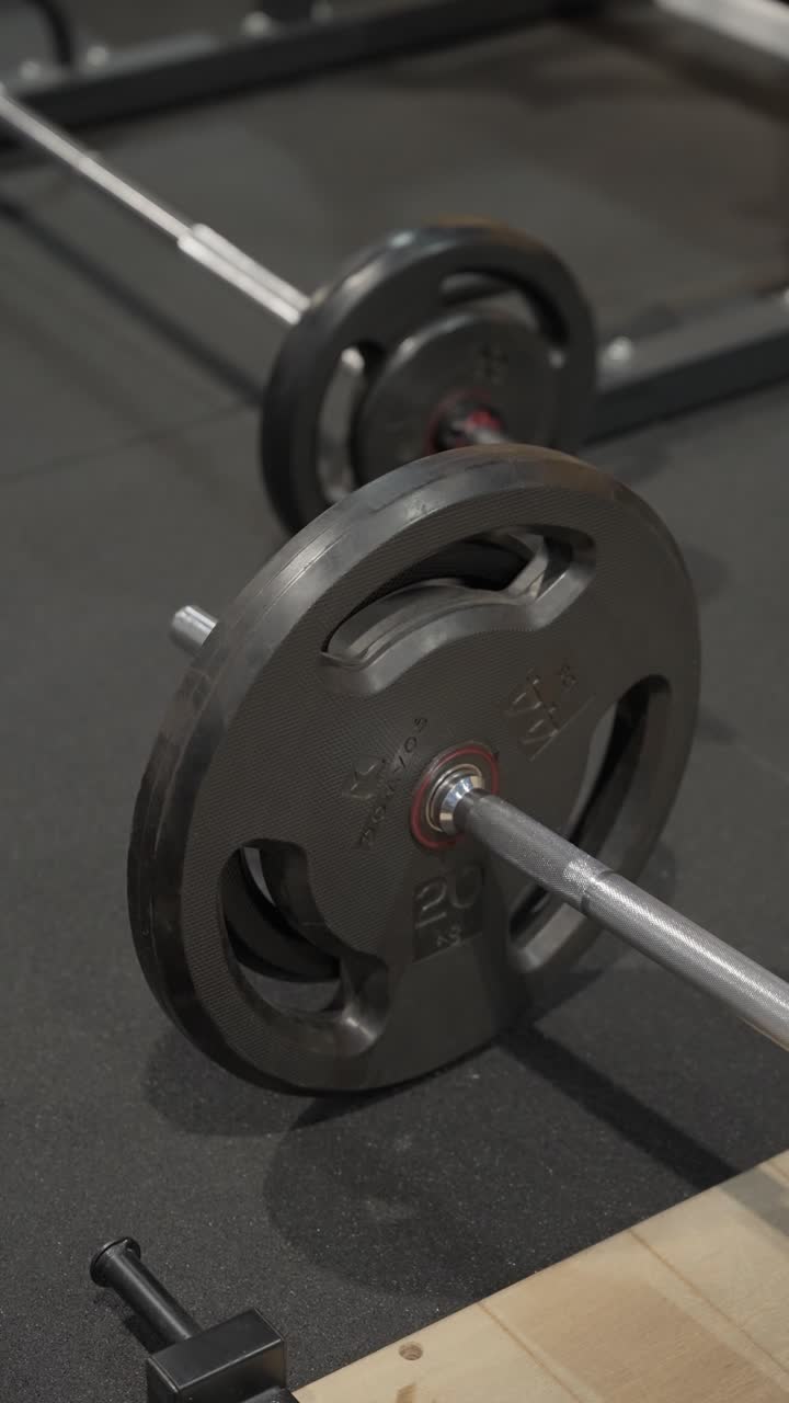 Primer plano de barra de pesas con discos de peso metálicos apoyados en el suelo de caucho de un gimnasio interior.