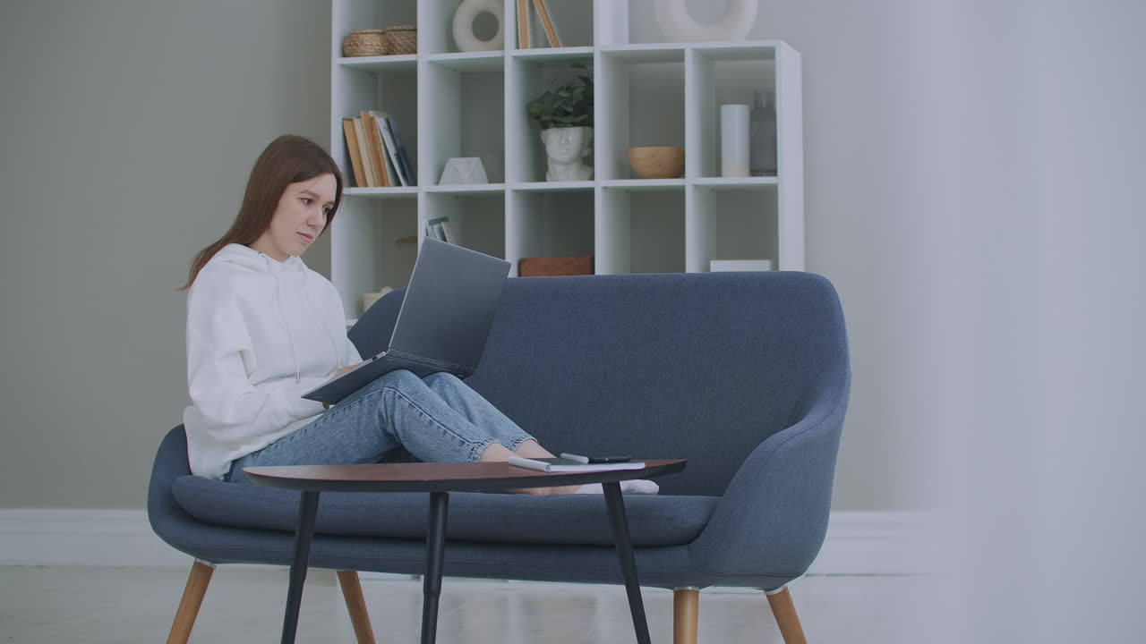 vista de bajo ángulo de una mujer sentada en un sofá mirando su computadora portátil. carrera independiente. mujer alegre trabajando en una computadora portátil sentada en el sofá en casa.