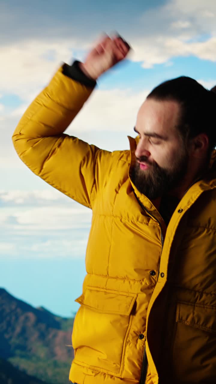 Hombre con chaqueta amarilla bailando felizmente en la cima de una montaña