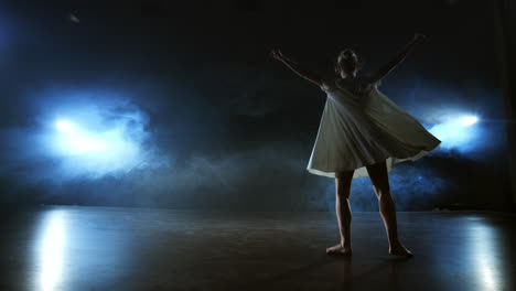 modern dance girl in a white dress dances a modern ballet jumps on the stage with smoke in the blue spotlights.