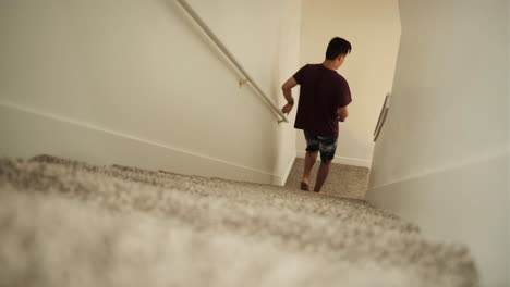 young man going down the carpeted stairs then sits on the floor