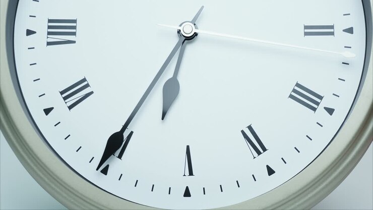 Time lapse silver wall clock short hand points on Roman numerals.
