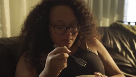 curly afro european woman eating out of bowl in the living room couch