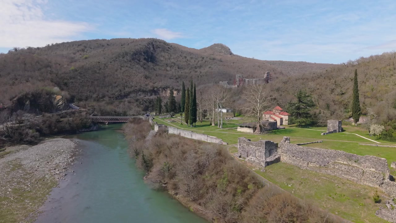 Riprese aeree in ascesa sopra la Fortezza di Nokalakevi, che svelano gradualmente le rovine storiche, la vegetazione rigogliosa, il fiume serpeggiante e la pittoresca campagna della Georgia occidentale.