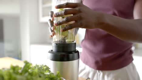 midsection of african american man preparing healthy smoothie in kitchen at home, slow motion