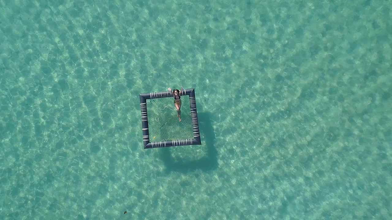 Girl relaxing in an inflatable pool in the ocean, Koh Kood, Thailand DRONE TOP DOWN FLY UP CROPPED