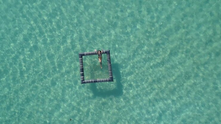 Girl relaxing in an inflatable pool in the ocean, Koh Kood, Thailand DRONE TOP DOWN FLY UP CROPPED
