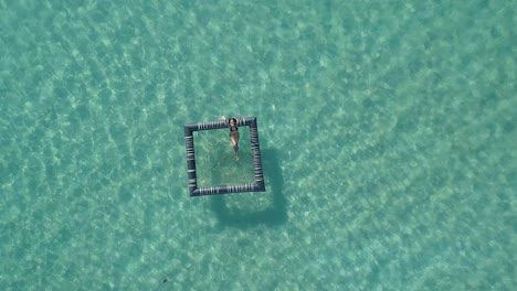 girl relaxing in an inflatable pool in the ocean, koh kood, thailand drone top down fly up cropped