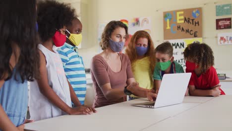 Lehrerin-Mit-Gesichtsmaske-Und-Computer,-Um-Kinder-In-Der-Klasse-In-Der-Schule-Zu-Unterrichten