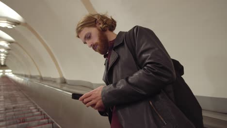 man using smartphone while standing on moving staircase