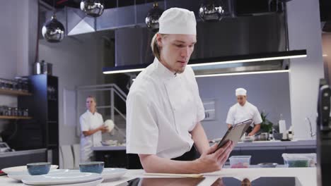 cocinero caucásico vestido con ropa blanca en una cocina de un restaurante usando una tableta