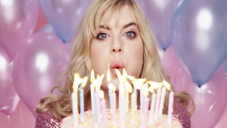 Beautiful-young-woman-blowing-out-candles-celebrating-birthday-pink-and-blue-balloon-background---Red-Epic-Dragon