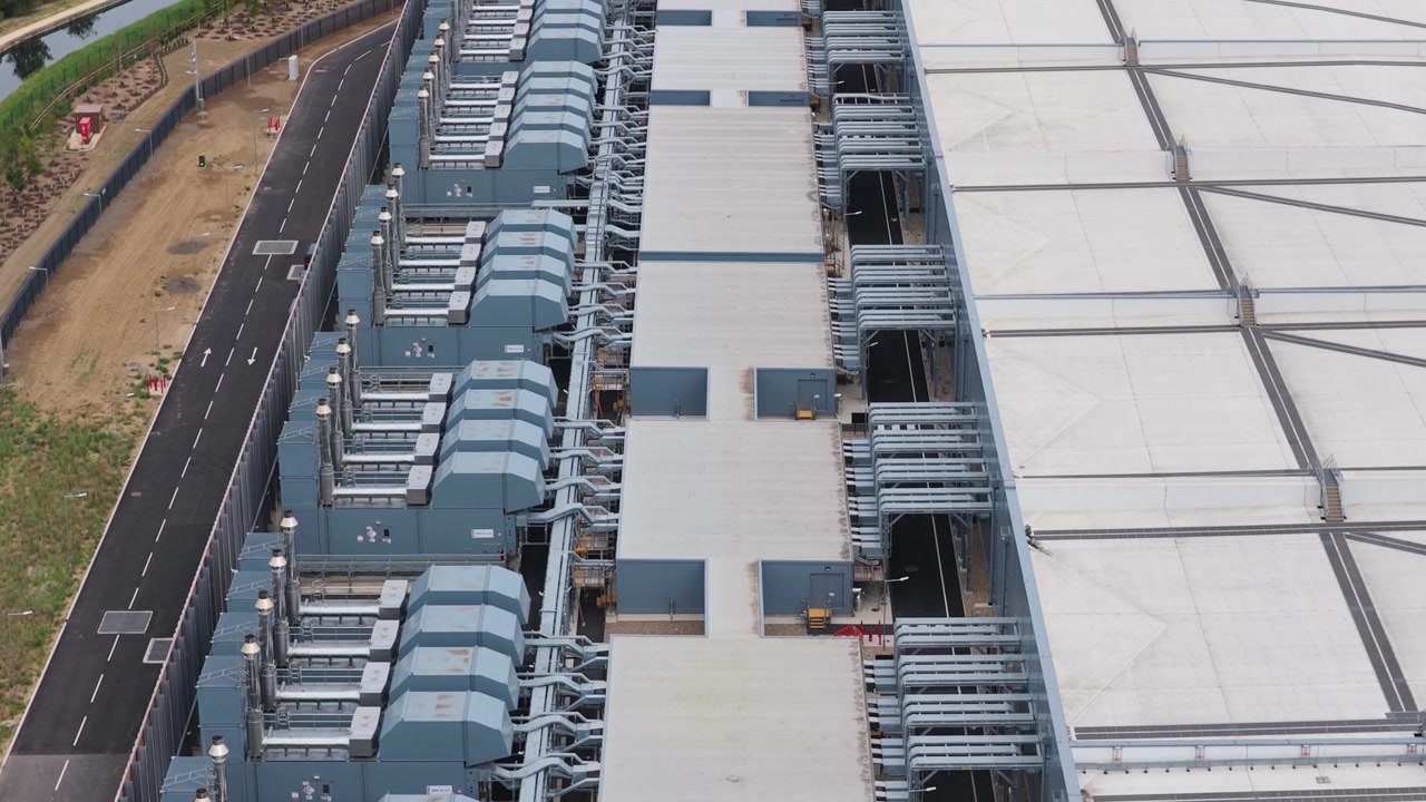 Stort industrielt datacenter eksteriør, der viser rækker af ventilationssystemer og køleenheder på en klar dag med asfalterede veje langs facilitetens struktur for vedligeholdelsesadgang.