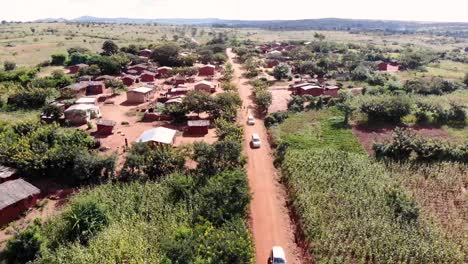 Turistas-Conduciendo-Coches-En-La-Carretera-De-La-Aldea-Africana-Rural,-Vista-De-Drones