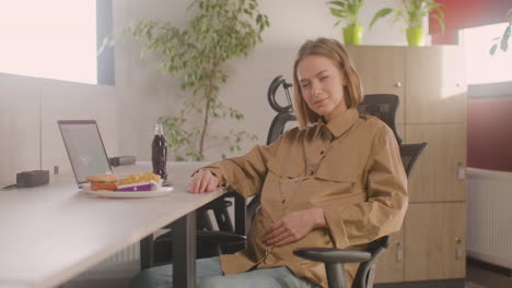 Working-Pregnant-Woman-Sitting-At-Desk-And-Smiling-At-Camera-During-Office-Lunch-Break