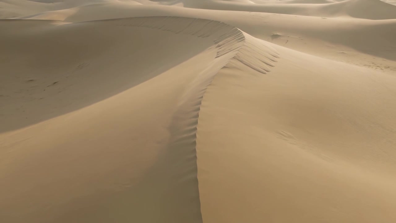 La telecamera drone che scivola rivela la cresta sinuosa di una duna di sabbia in un erg desertico, evidenziando le increspature.