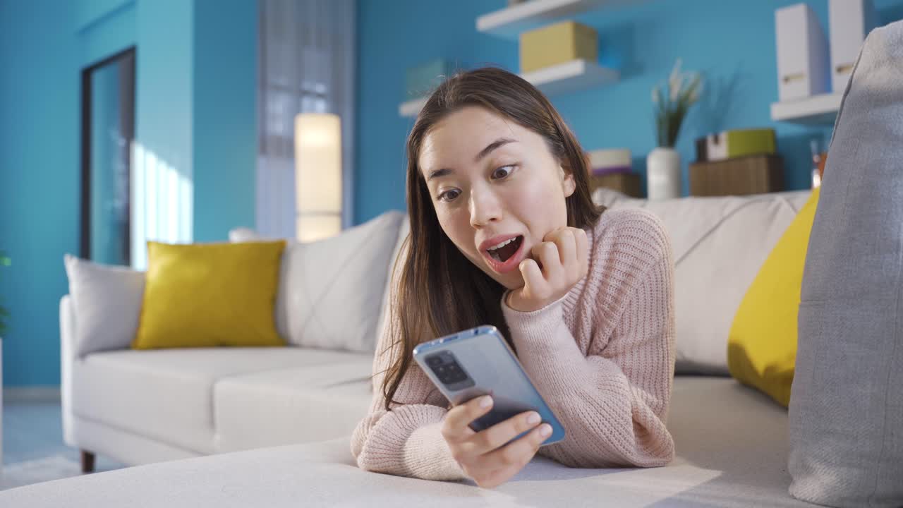 행복한 아시아 십대 소녀가 집에서 스마트 폰을 사용하고 있습니다.