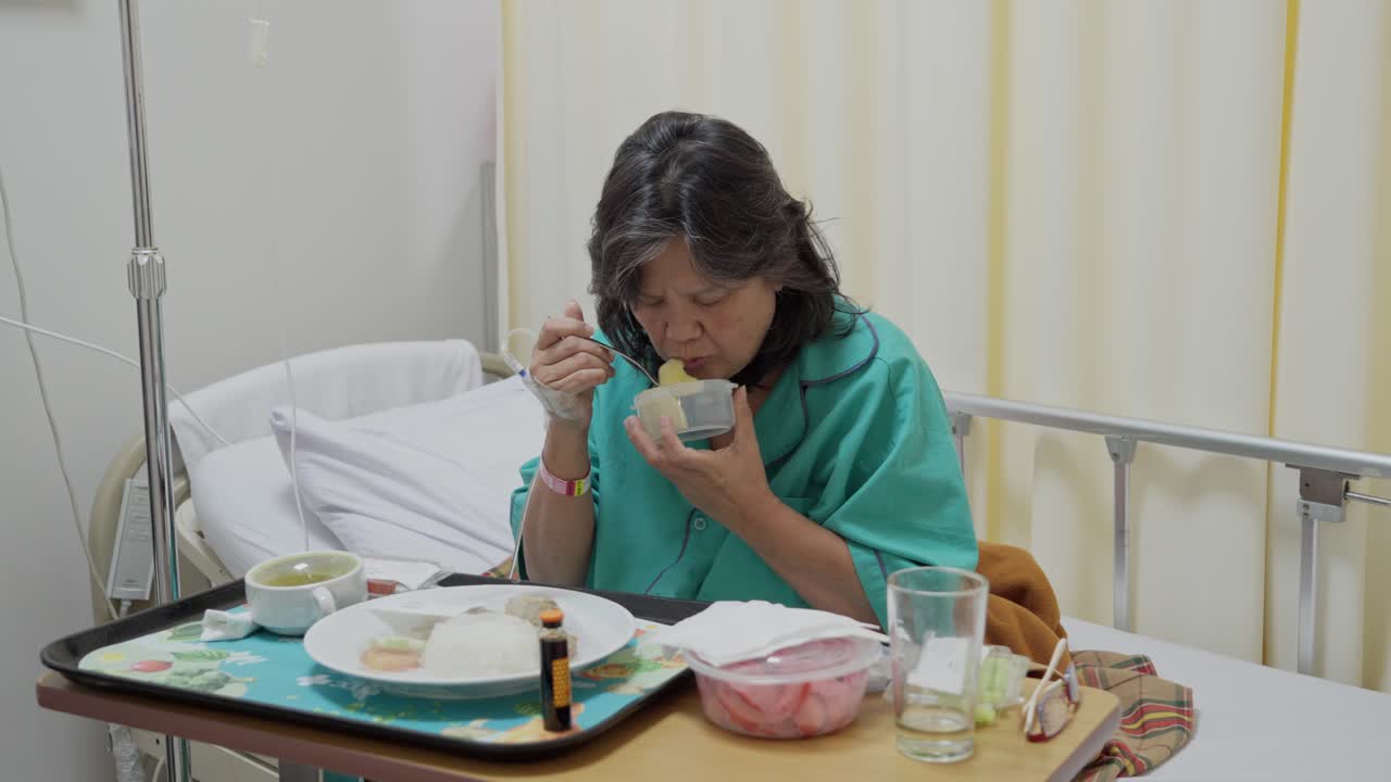 Elderly woman eating hospital food alone in a patient room, looking focused and serious