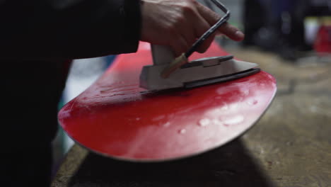 ironing hot wax onto base of red snowboard