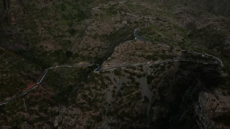 Vista-Aérea-En-Una-Carretera-Serpenteante-Con-Coches.-Vuelo-Aéreo-Sobre-Una-Carretera-Serpenteante-Más-Allá-De-Las-Montañas-Cubiertas-De-Verde-Y-Marrón