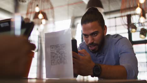 Mixed-race-man-giving-african-american-female-cafe-worker-his-smartphone-in-order-to-pay