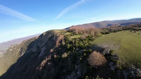 drone hovering over the peak of a rocky mountain covered in lush green trees. sunny day with a blue sky. relaxing slow-motion image, evoking depth and conveying the tranquility of nature