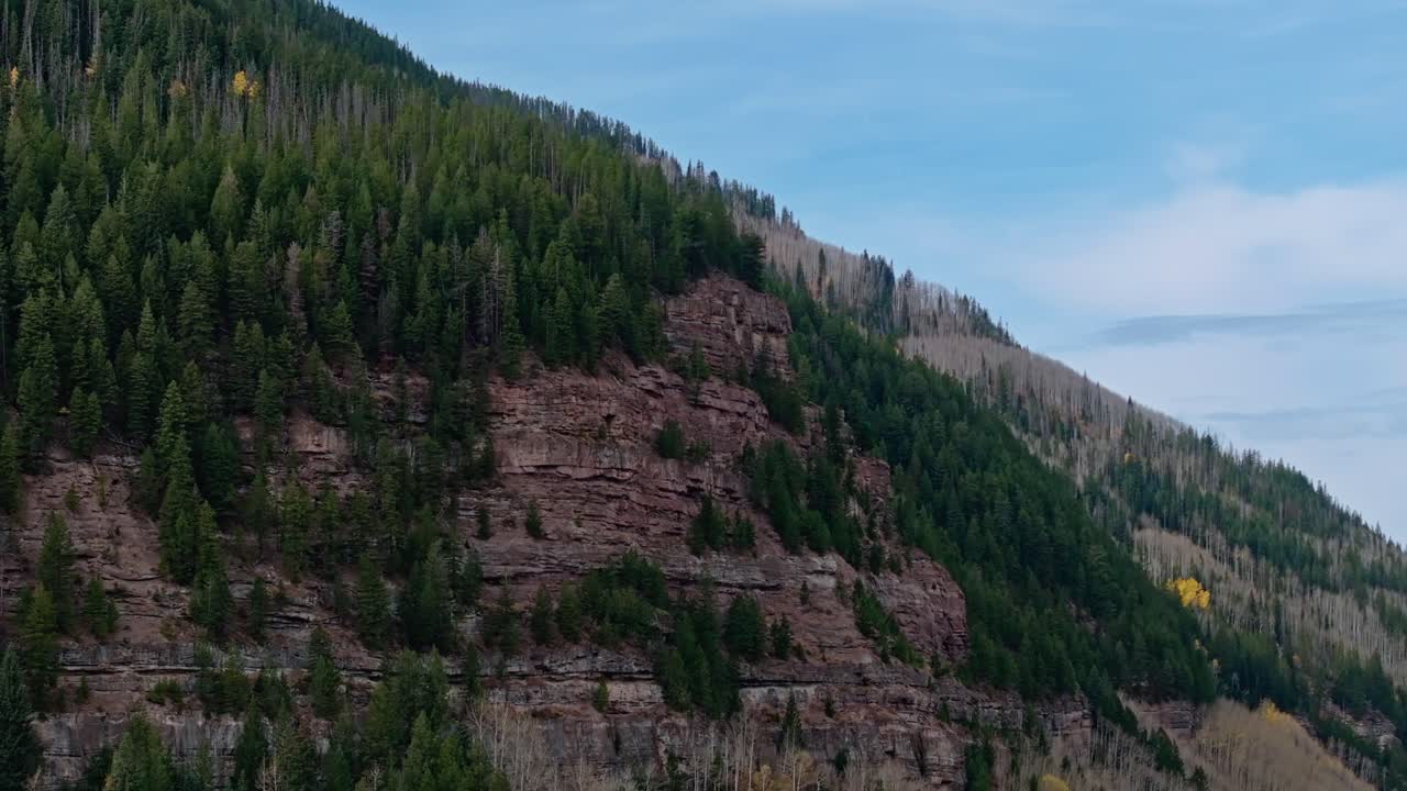 Majestic cliffs and lush green trees on a bright day, showing Vail's rugged natural beauty, aerial orbit establishing