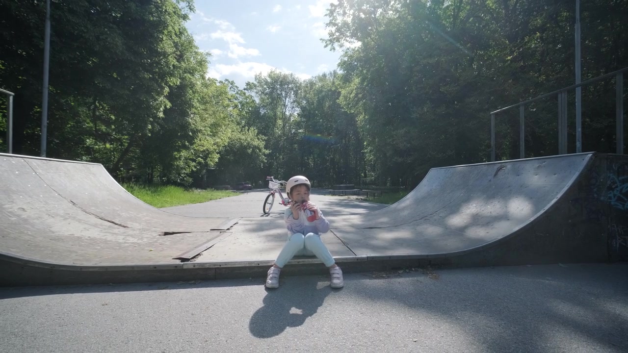 Bambina con il casco seduta che mangia un gelato in uno skate park