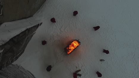 people in red clothes circling a bonfire on snow