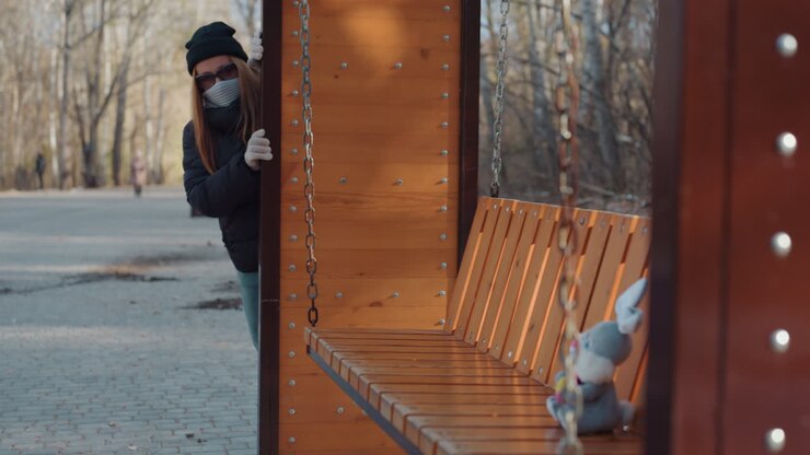 Suspense builds in quiet park. Hidden watcher scans soft toy beneath dim outdoor lighting. An enigmatic presence carefully observes plush toy while concealed behind trees in shadowed park