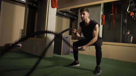 strong athlete doing battle rope exercise at crossfit gym