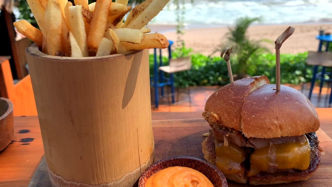 vista panorámica de hamburguesa con queso y papas fritas con vista al mar, filmada en seminyak, bali, indonesia