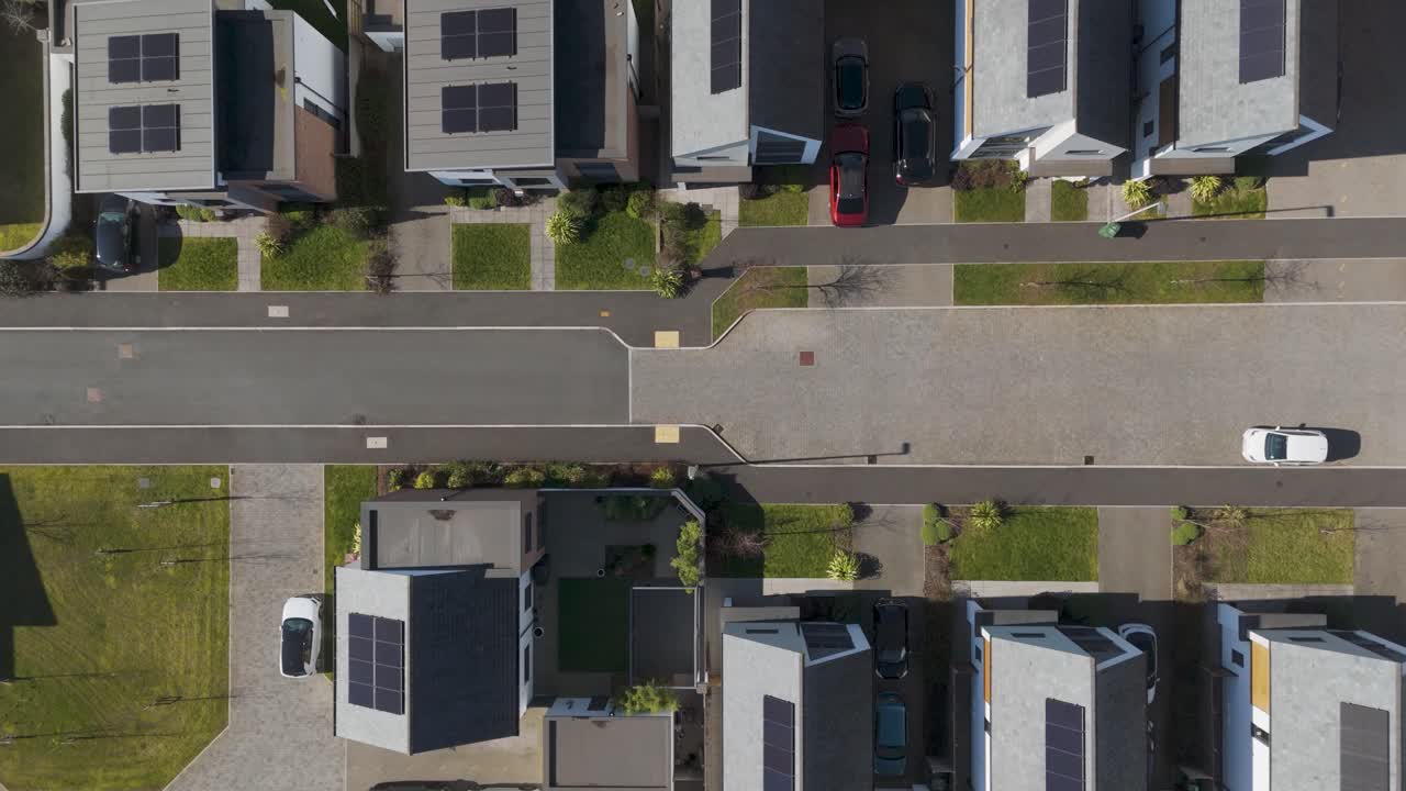 Top-down aerial of luxury eco-estate with white modern homes, dark solar-panel roofs, manicured lawns and precise street grid showcasing upscale sustainable suburban design