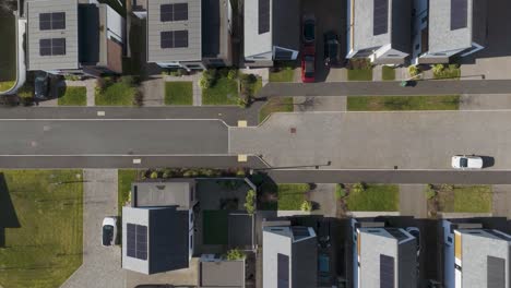 top-down aerial of luxury eco-estate with white modern homes, dark solar-panel roofs, manicured lawns and precise street grid showcasing upscale sustainable suburban design