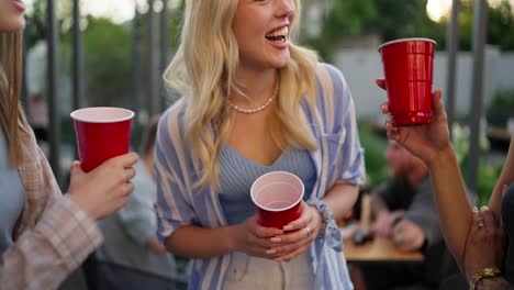 Close-up-a-trio-of-girls-holding-plastic-red-glasses-in-their-hands-communicate-and-have-fun-during-their-party-in-the-courtyard-of-a-country-house