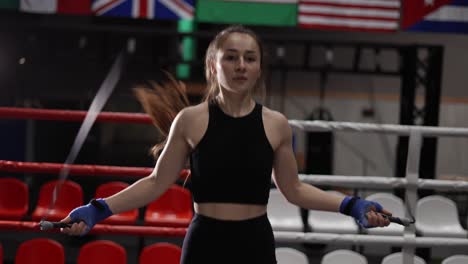 mujer joven en un top deportivo negro con una cuerda de saltar en un gimnasio de boxeo en el ring