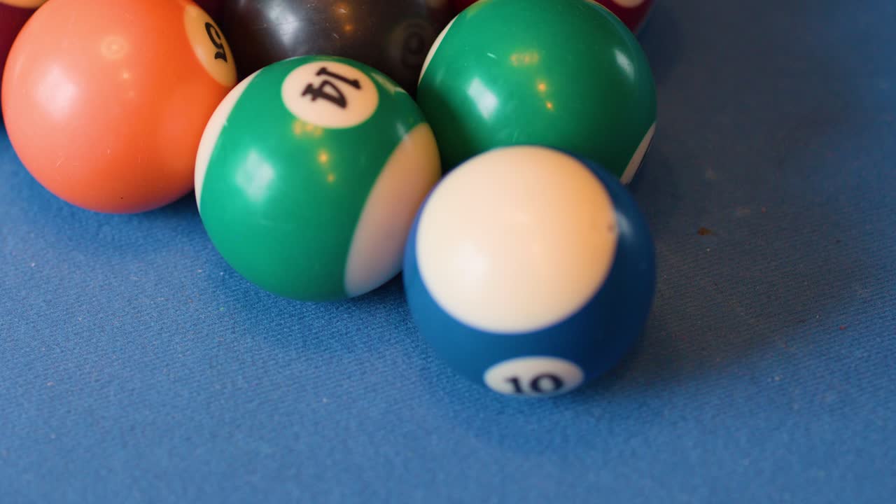 Multiple billiard balls collide and scatter across a blue felt pool table under even lighting