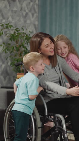 cute children snuggle up to mom in wheelchair to make selfie on modern tablet. woman with disability has fun with son and daughter in living room