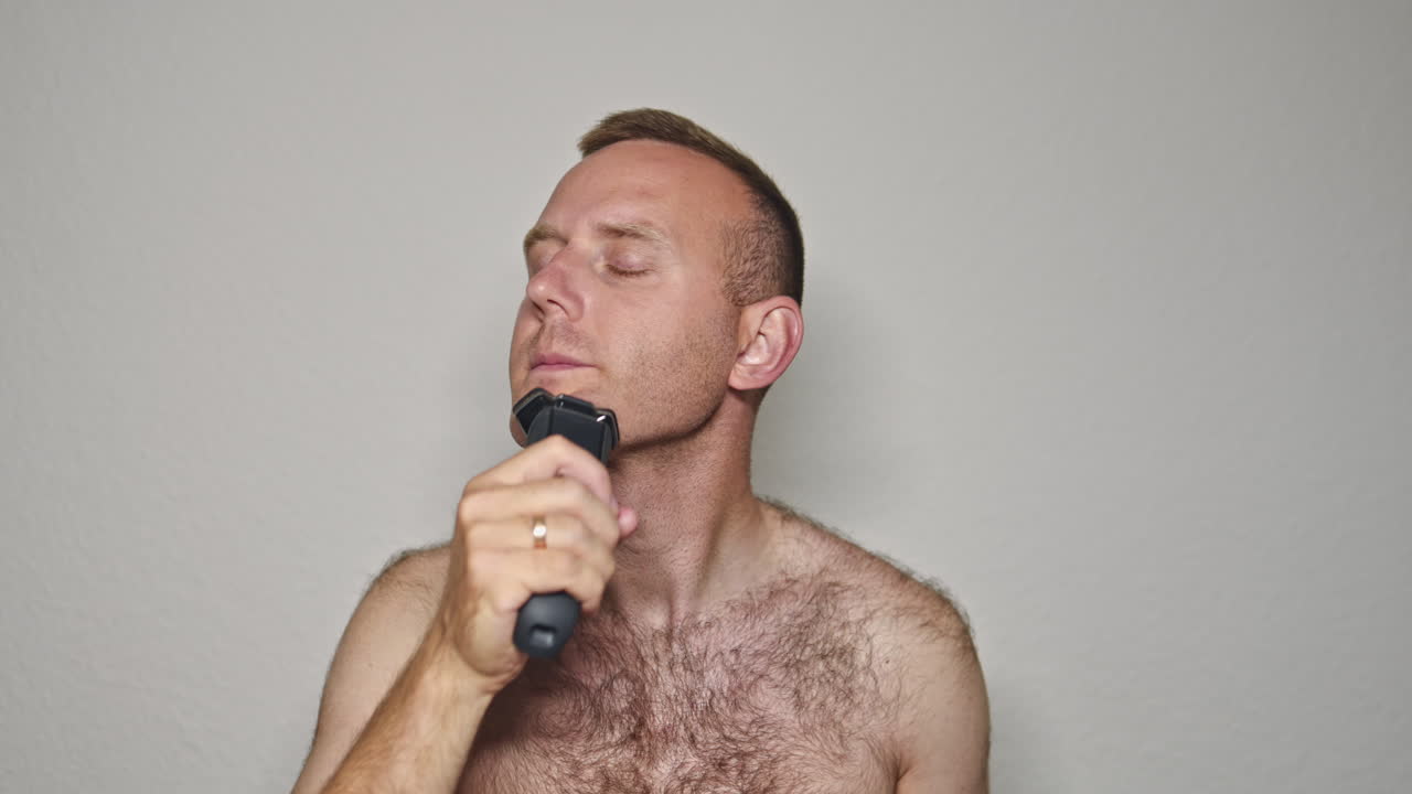 Primo piano di un uomo con un rasoio tra le mani che si rade la barba. Igiene facciale maschile, radendo la barbetta. Un uomo si rade il viso allo specchio