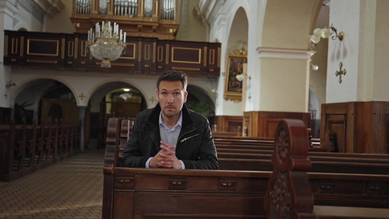 Uomo in cerca di pace in una chiesa, seduto su una panca di legno per pregare, circondato dal silenzio e da una luce naturale soffusa.