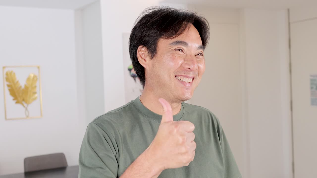 A man in a green shirt smiles and gives a thumbs up in a well-lit room