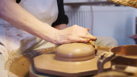 primer plano de un alfarero masculino arrojando arcilla para una olla en una rueda de cerámica en un estudio de cerámica