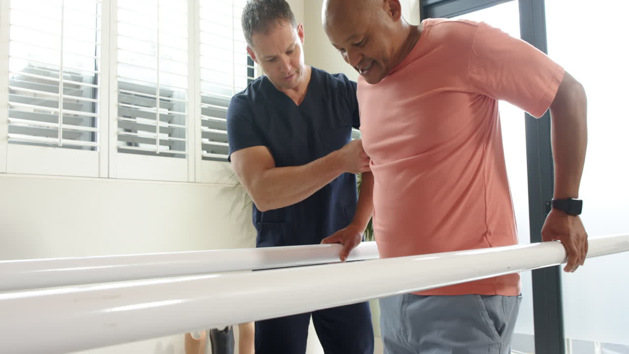 Therapist assisting man walking with prosthetic leg on parallel bars indoors