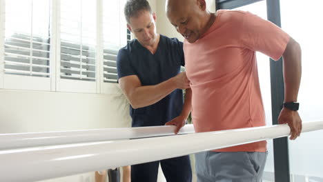 therapist assisting man walking with prosthetic leg on parallel bars indoors