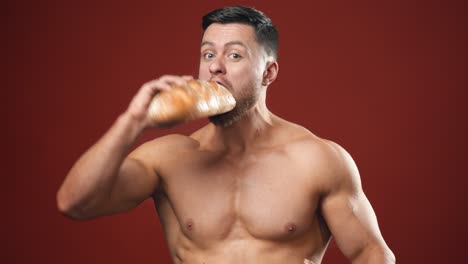 hungry strong male eating unhealthy food. half-length portrait of muscular man without shirt eats bread and sausage quickly on the studio background.