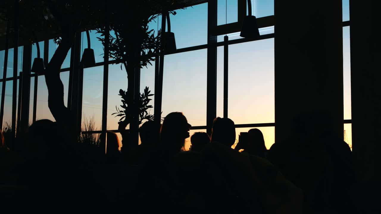 창문으로 볼 수 있는 레스토랑에서 해가 지는 것을 지켜보는 사람들의 실루