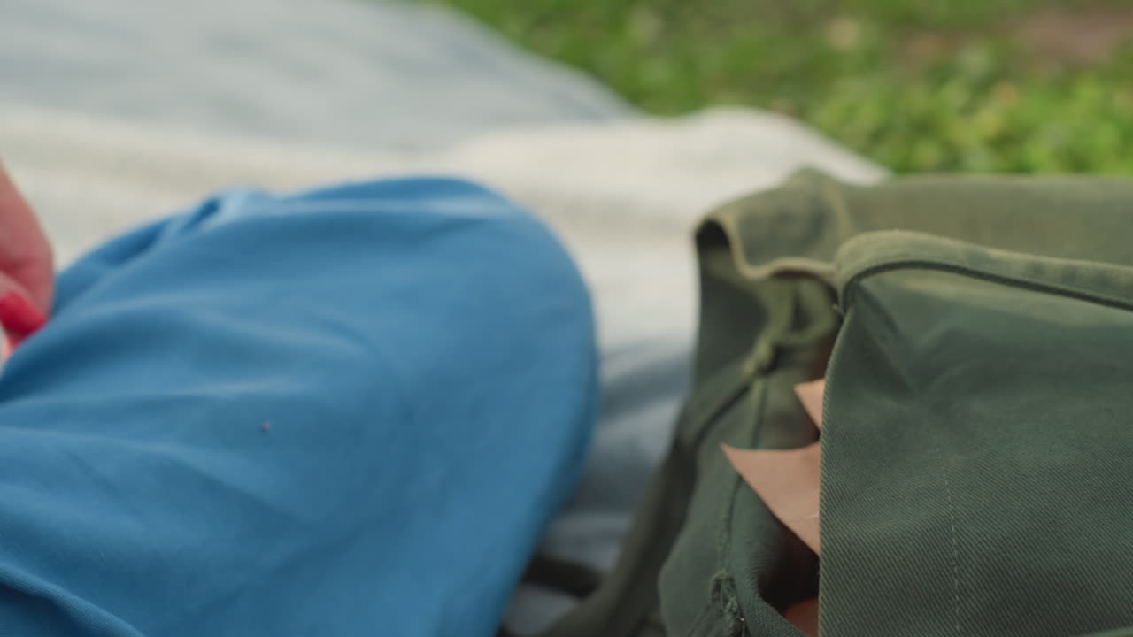 mom hand reaching into olive canvas bag on picnic blanket pulling out snacks, warm sunlight on arm, soft blur background of green grass creating calm outdoor family moment