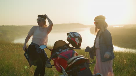 two friends are having fun while cleaning a motorcycle in a scenic field, one is wiping the back seat of the bike, while the other dances happily in the sunset