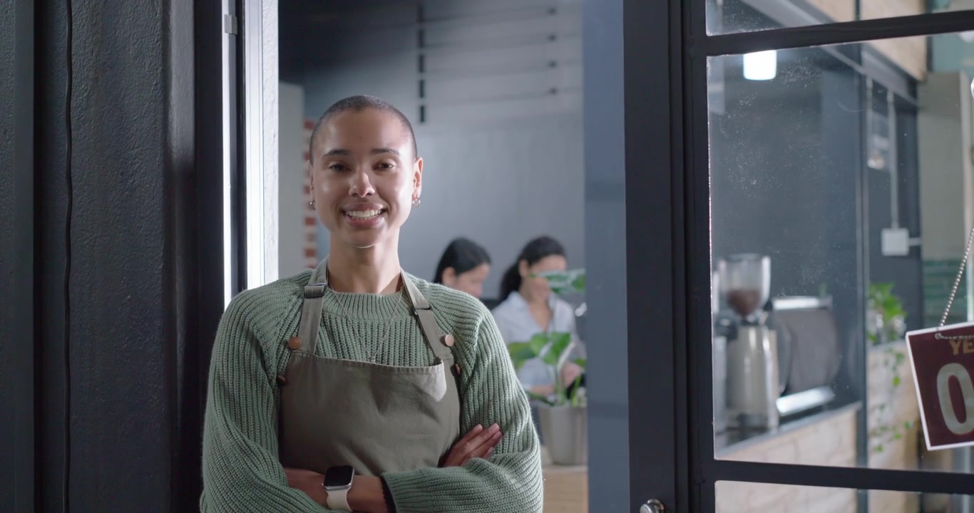 Barista afroamericano con grembiule che gira il cartello "CHIUSO" e apre la porta del caffè, con spazio per il testo.