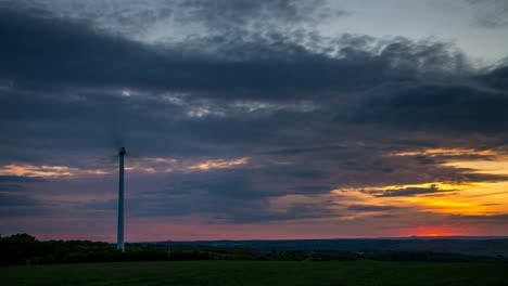 Sunset-Timelapse,-dramatic-clouds-and-landscape,-fast-rotating-wind-turbine-in-foreground